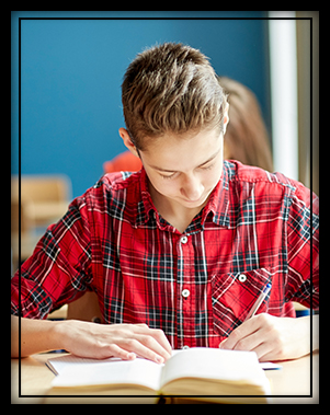 High school student in red flannel working at his desk in the classroom