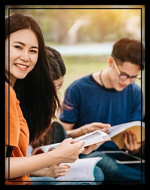 Happy female college student studying outside with classmates